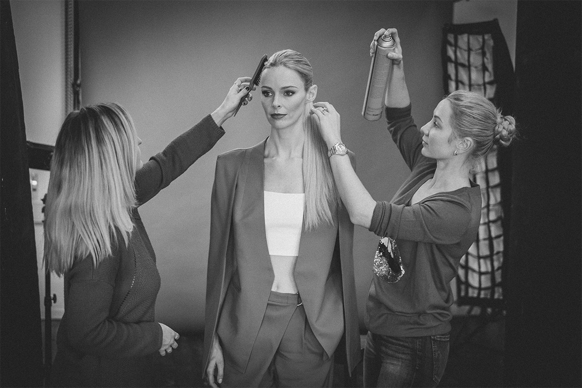 Hair Extensions |A black and white image of two blonde women fixing their model's ponytail hairstyle with combs and hairspray.