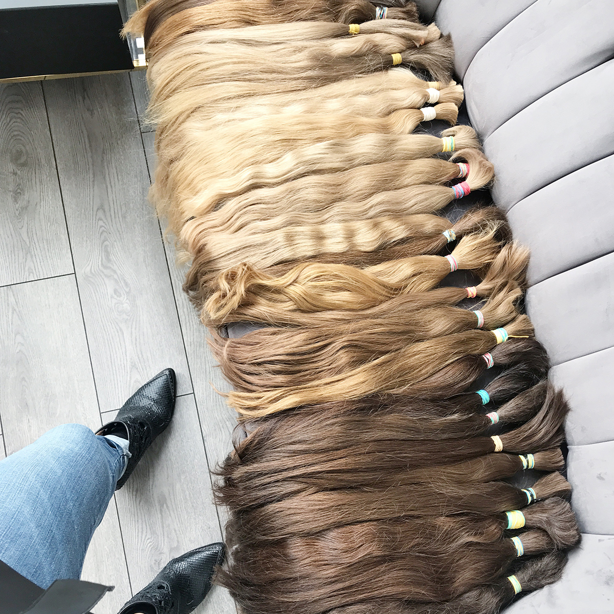 Slavic Virgin Hair Extensions |Different coloured cut out ponytails laid on a grey suede sofa.